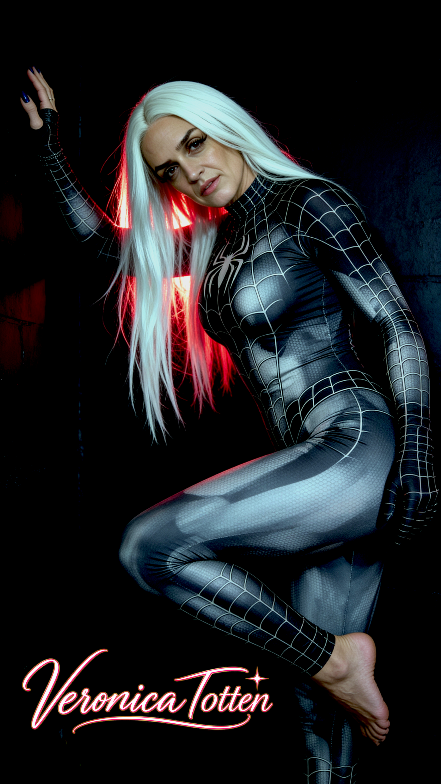 Veronica Totten in a black spider suit, seated cross-legged and holding a glowing red cube